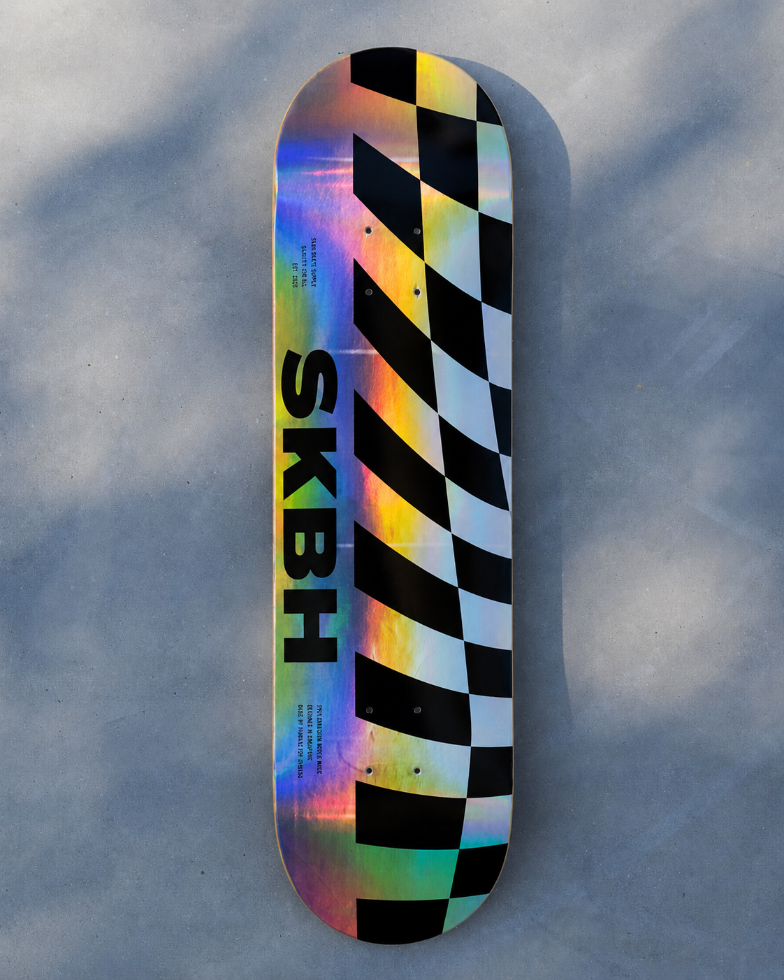 A skateboard deck with a black and white checkered pattern on one side and a holographic iridescent finish on the other, featuring the bold black text 'SKBH' printed vertically. The deck is photographed from directly above on a gray concrete surface with soft shadows.