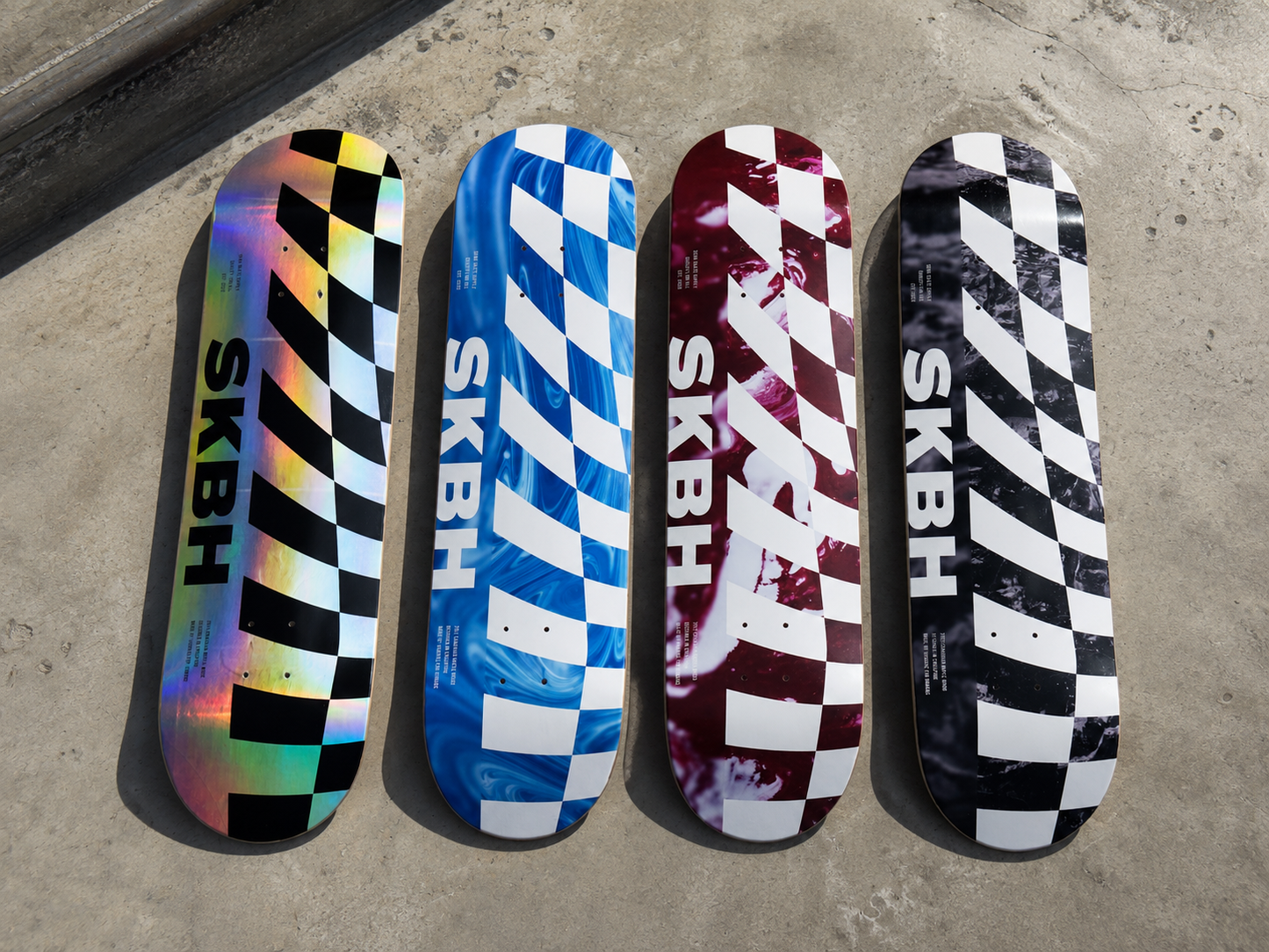 Four skateboard decks lined up vertically on a concrete surface, each featuring a different graphic design: holographic black-and-white checkers, blue-and-white checkers, maroon-and-white checkers with a splatter effect, and black-and-white checkers. The brand name SKBH is printed vertically on each deck.